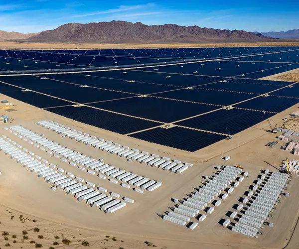 Aerial view of huge solar power farm next to white storage buildings.